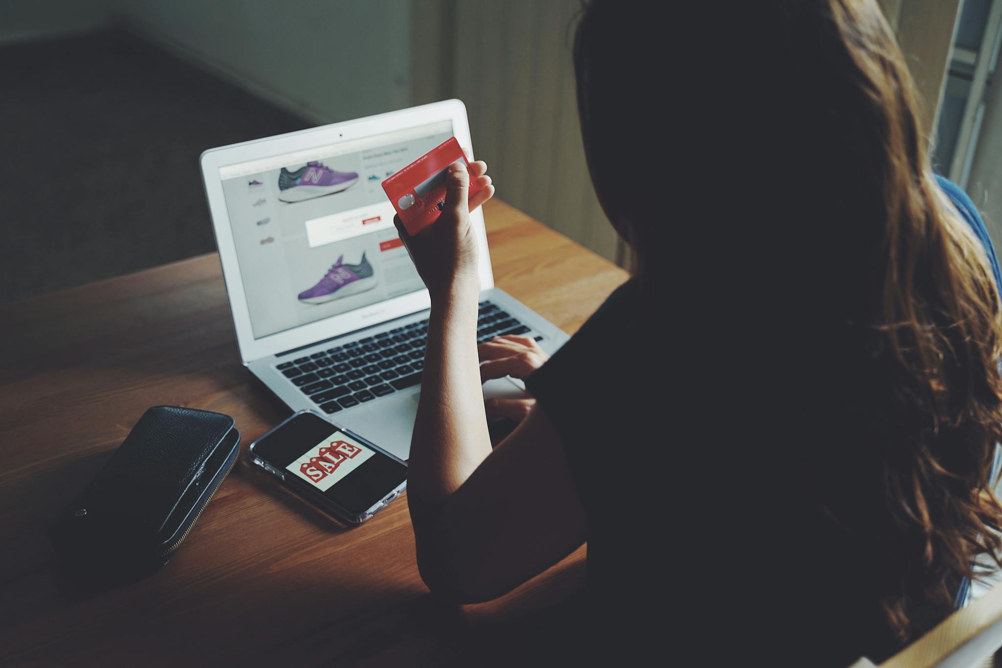 A woman shops online using a laptop and credit card on a wooden table.